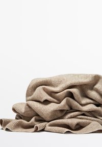 Tissu tricoté beige, drapé lâchement avec des plis, présentant une texture douce et des bords côtelés. Fibres naturelles avec des variations de couleur subtiles.