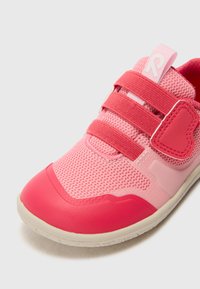 Pink athletic shoe featuring mesh material with elastic straps, a rubber toe cap, and a heart-shaped accent on the side. White outsole.