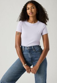 T-shirt ribbed di un leggero colore lavanda con scollatura a girocollo e maniche corte, abbinato a jeans in denim blu a vita alta. Dettaglio del logo sobrio sul petto.