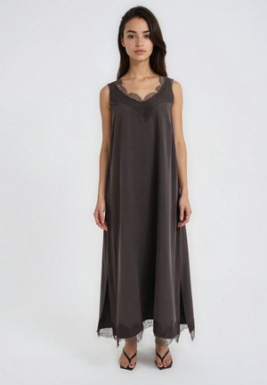 Woman wearing a sleeveless dark gray long dress with lace trim at neckline and hem, standing with hands relaxed by sides on a white background.