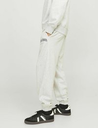 Pantaloni sportivi grigi in cotone con polsini elastici, tasche laterali e dettaglio del logo sulla coscia sinistra. Indossati con scarpe da ginnastica nere e bianche.