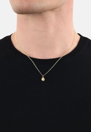 Goldene Halskette mit einer dünnen Kette und einem kleinen, runden Anhänger mit strukturiertem Oberflächen, getragen über einem schwarzen Shirt.
