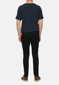 Granatowa koszula z krótkim rękawem, czarne spodnie w wąskim kroju oraz brązowe, casualowe buty. Koszula ma prosty design i miękką teksturę.