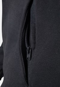 Chaqueta negra con cremallera que presenta una textura de tela suave, detalle de cremallera en contraste y una apertura en ángulo para un acceso funcional.