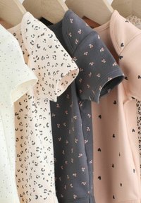 Négy rövid ujjú bababody fa vállfákon, krémszínű, fehér leopárdmintával, sötétszürke cseresznyékkel és őszibarackszínű szívmintákkal.