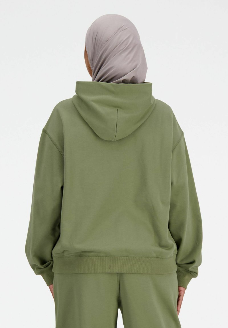 Olijfgroene oversized hoodie met een capuchon, verlaagde schouders en geribbelde manchetten. Zachte textuur, minimalistisch ontwerp, gedragen met bijpassende onderstukken.