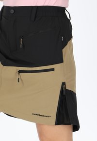 Two-tone skirt featuring black and tan sections, made of lightweight fabric, with zippered pockets on both sides and a partially elastic waistband.