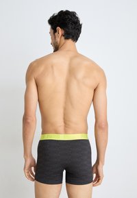 Black boxer shorts with a textured pattern, featuring a bright yellow elastic waistband branded "PUMA." Back view shows a fitted design.