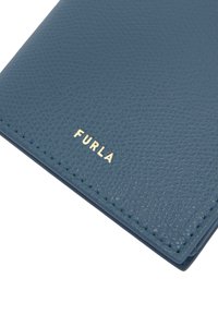 Textured blauwe leren portemonnee met gouden "FURLA" logo aan de onderkant. Het heeft zichtbare stiksels en een strak, rechthoekig ontwerp.
