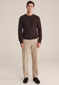 Brūns adīts džemperis ar ribotu tekstūru, saskaņots ar gaiši bežām biksēm un tumši brūnām kurpēm. Vienkāršs, ikdienas dizains ar apaļu kakla izgriezumu.