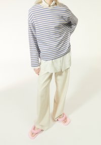 Sweter w paski w kolorze beżowym i lawendowym, noszony na białej koszuli. Dopełnieniem stylizacji są jasne spodnie o szerokich nogawkach oraz różowe, masywne klapki.