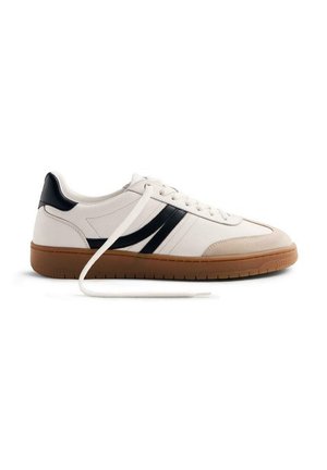 Zapatilla blanca con rayas negras, con una parte superior texturizada y una suela de goma. Los cordones son blancos, con un diseño liso y punta redondeada.