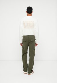 Λευκό T-shirt με μακριά μανίκια και εκτυπωμένο κείμενο στην πλάτη, συνδυασμένο με ελιξόχρωμο cargo παντελόνι με πλαϊνές τσέπες και ίσια γραμμή.