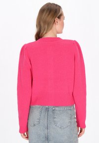 Fuksijasti pleten pulover z rebrastim ovratnikom in robom, z nabranimi rameni in skrajšanim dizajnom. Nosi se čez svetlo jeans krilo.
