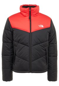 Giacca a vento nera e rossa, con colletto alto, chiusura con zip e motivo a chevron trapuntato sul corpo. Logo in alto a sinistra.