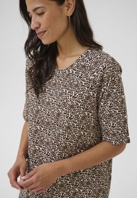 Top s leopardím vzorom v svetlej béžovej a hnedej farbe, s krátkymi rukávmi, okrúhlym výstrihom, z mäkkého materiálu, s voľným strihom a jemnými záhybmi.