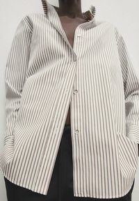 Randig skjorta i ljusbeige och brun bomull, med knappstängning framtill, spetsig krage och sidofickor. Avslappnad passform med lång ärm.