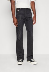Vaqueros de mezclilla negra con corte recto, decoloración sutil, costuras en contraste y bolsillos frontales. Combinados con zapatillas negras.