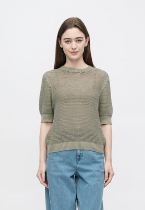 Maglione a maniche corte di colore verde oliva, lavorato a maglia con vestibilità ampia, orlo a coste e motivo a rete dettagliato, indossato con jeans a gamba larga azzurri.