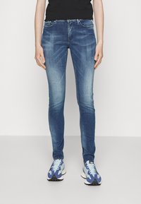 Vaqueros de mezclilla en azul oscuro, con un ajuste slim, detalles desgastados en los muslos, diseño de cinco bolsillos y una clásica cremallera con cierre de botón.