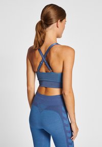 Blå sportbehå med korsade axelband, texturerad tyg och sömlös design. Kombinerad med högmidjade leggings med geometriska mönster.