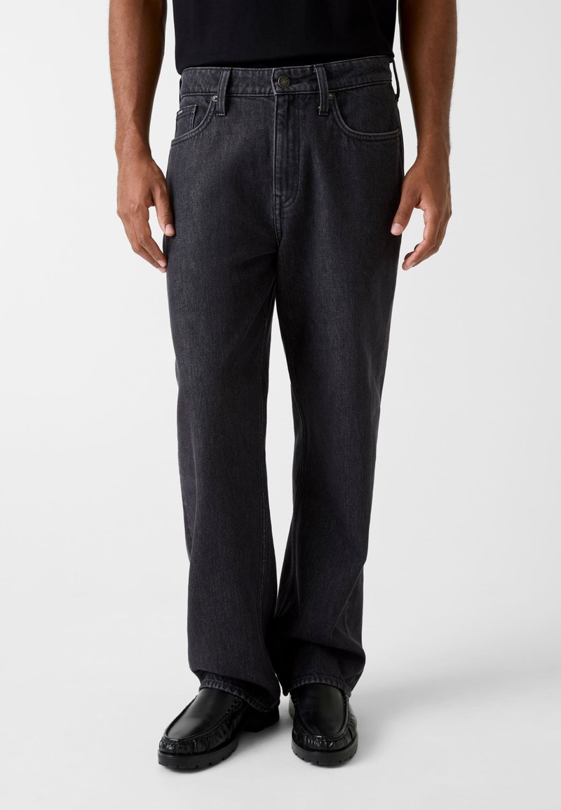 Donkergrijze spijkerbroek met een relaxte pasvorm en rechte pijpen. Voorzien van steekzakken aan de voorkant, een knoopsluiting en subtiele stikseldetails.