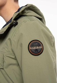 Lichtgroene jas van nylon, met een gestructureerde patch op de schouder met een zwart en oranje logo en een koordkap.