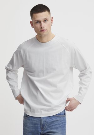 Weißes Langarm-T-Shirt mit Rundhalsausschnitt und Raglanärmeln. Glattes Baumwollmaterial, lockere Passform, kombiniert mit lässigen blauen Jeans.