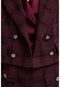Veste en tweed bordeaux avec un motif à carreaux, design croisé, boutons floraux en argent et doublure intérieure lisse couleur bordeaux.