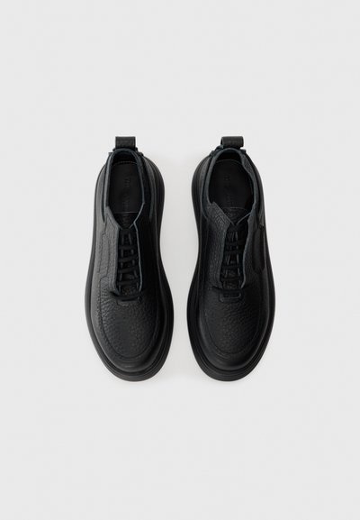 Pair of black textured leather lace-up shoes with rounded toes and thick soles on a plain light background.