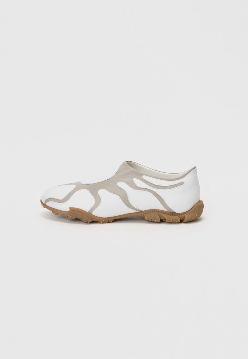 Botte de sport avec une tige blanche et beige clair présentant un motif ondulé, un col élastique semblable à une chaussette et une semelle en caoutchouc texturé.