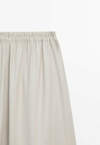 Jupe beige clair avec une taille élastique, tissu lisse et plis doux sur fond blanc.