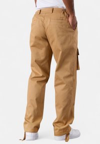 Relaxed-fit khaki cargo pants with elastic waistband, side pockets, and drawstring details at the hem. Made of sturdy cotton material.