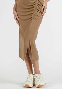 Braunes tailliertes Midikleid mit seitlicher Raffung, einem Schlitz vorne und einer glatten Textur, kombiniert mit klobigen weißen Sneakers mit orangen Akzenten.