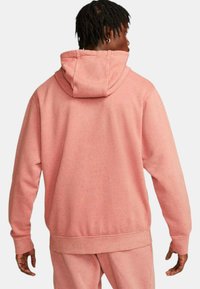 Różowa bluza z luznym krojem, teksturowanym materiałem, kapturem na sznurku i ściągaczami przy rękawach. Posiada wzór w plamki oraz kieszeń kangurkę.