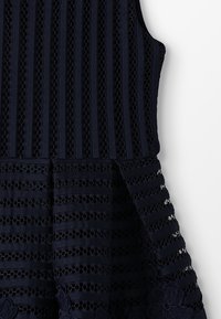 Mekko, joka on meritummansininen ja jossa on teksturoitu kuvio, joka koostuu vuorottelevista raidoista ja mesimarja-rei'istä; hihassa on kukkaistikuvio. 