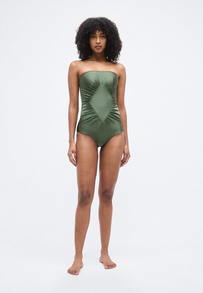 Ολόσωμο μαγιό χωρίς τιράντες σε ελιά πράσινο με υφασμάτινο διακοσμητικό μοτίβο ρόμβου στο κέντρο. Μαλακό ύφασμα με λείο φινίρισμα. Μινιμαλιστικός σχεδιασμός.