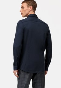 Chemise marine à manches longues, avec des poignets à boutons et un col propre. Tissu lisse avec une coupe ajustée, associée à un pantalon à carreaux gris.