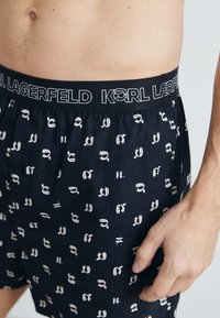 Čierne boxerky s opakovaným vzorom bielych grafických tvárí a logom. Majú elastický pás s brandingom "KARL LAGERFELD".