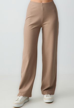Pantalons marron taille haute avec des rayures verticales blanches. Conception à jambes larges en tissu lisse, associés à des baskets blanches.