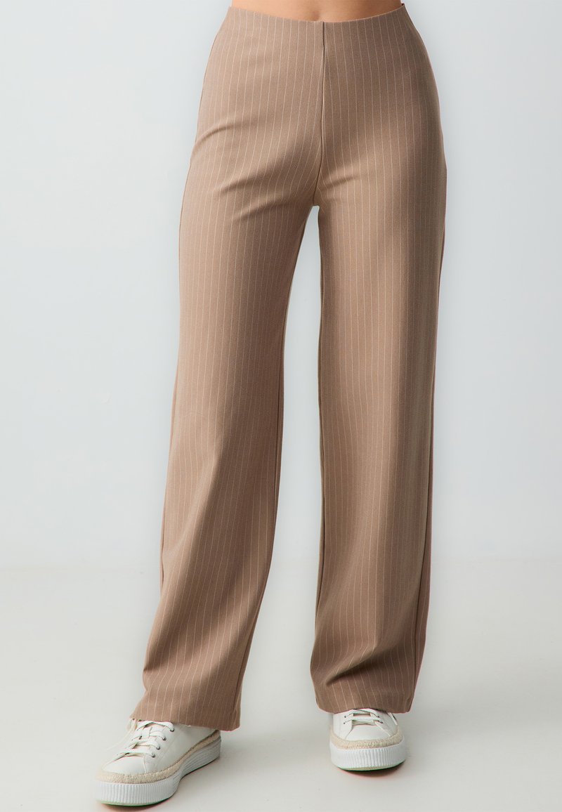 Bruine, high-waisted broeken met witte verticale strepen. Brede pijpen gemaakt van soepele stof, gecombineerd met witte sneakers.