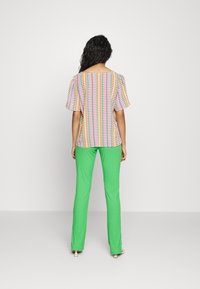 Top texturizado e multicolorido com padrões geométricos, combinado com calças justas verdes brilhantes. Fundo simples, modelo visto de costas.