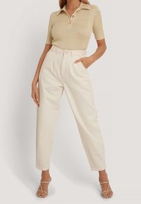 Polo beige à côtes avec manches courtes et deux boutons, associé à un pantalon en toile couleur crème taille haute et des sandales beige à brides.