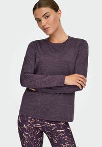 Langærmet lilla top med rund hals og struktureret overflade, parret med mønstrede tights i brune og hvide farver.