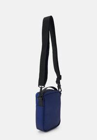 Borsa a tracolla blu navy con una tracolla nera. Caratteristiche di materiale liscio, forma rettangolare, manico superiore e accessori regolabili.