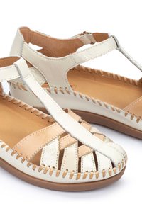 Sandalias de cuero ligeras con colores beige y blanco roto, diseño de tiras en T, detalles tejidos y acentos cosidos en una suela plana.