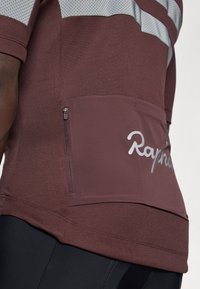 Bordový cyklistický dres s šedými akcenty, krátký rukáv, zipová kapsa na zadní straně a odrazové detaily. Obsahuje stříbrné logo "Rapha".