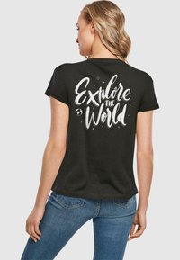 Sortærmet sort t-shirt med hvid skrift i kursiv "Explore the World" på ryggen, med et globus-ikon og små dekorative prikker.