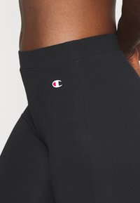 Svarta leggings med hög midja, tillverkade av stretchigt tyg. Har en liten Champion-logotyp i röd och vit på den nedre sidan.