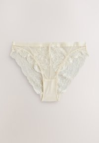 Culotte bikini en dentelle crème avec motif floral et bords festonnés, posée à plat sur un fond clair.